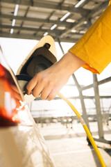 Woman hands attaching power cable supply to charge electric or EV car on the solar panels...