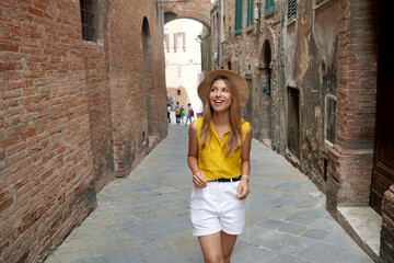 Holidays in Tuscany. Beautiful stylish tourist girl walking between narrow alleys of Siena historic town of Tuscany, Italy. - obrazy, fototapety, plakaty
