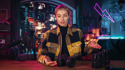 Attractive Young Female Recording a How To Video About New Photo Camera and Video Equipment. Entertaining Woman with Short Hair Explaining New Features on Live Podcast on Social Media.