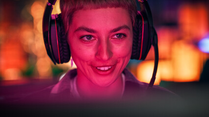 Close Up Portrait of a Stylish Young Female with Short Hair Playing Online Computer Video Game in the Evening at Home. Gamer Discussing Tactics with Teammates while Talking into Headset.
