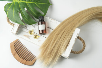 A natural essential oil or serum for hair care lying on a white wooden tray. Hair care and smoothing concept