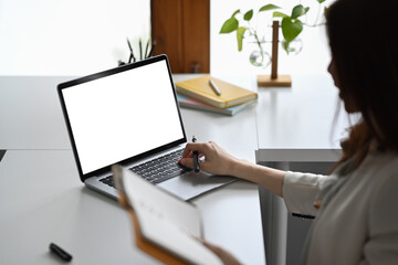 View over shoulder businesswoman holding notebook and using laptop at her office desk