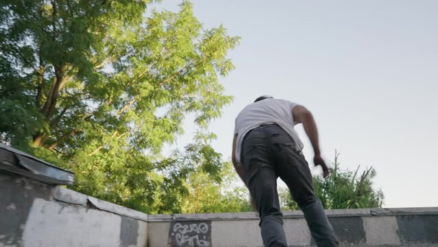 Male parkour athlete performs a trick with overcoming obstacles. Makes a distance jump and lands in a somersault. Slow motion.