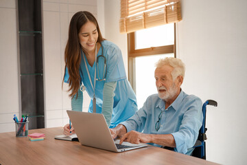 Friendly young woman nurse helping senior man in wheelchair using laptop, Elderly male patient surfing on Internet at nursing home.