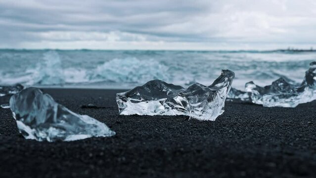 Close-up of beautiful iceberg on black sand at Diamond beach in Iceland. Chunks of floating ice from Jokulsarlon glacier lagoon. Scenic view of waves rushing at sea shore in Iceland.