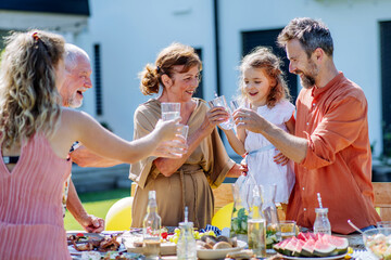 Multi generation family having garden party celebration, toasting and laughing.