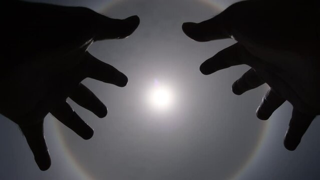 Aerial view of the sun with a circular rainbow surrounded by bright skies and white clouds with shadows of outstretched hands. Phenomenon, sun halo. Natural background in motion. drone shooting sun an