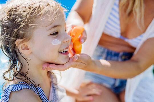 Close-up of young mother applying and sunscreen lotion to her daughter. People skin protection. Safety sunbathing in hot day.