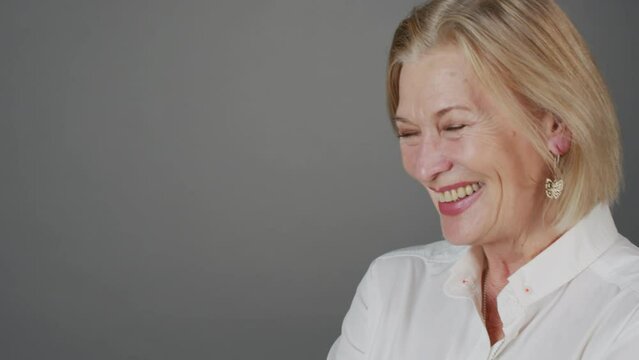 Closeup portrait of attractive adult Caucasian woman laughing at camera posing at grey background