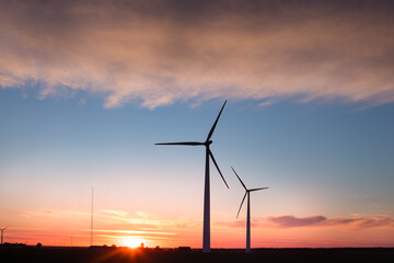 Fototapeta premium Wind farm in agricultural landscape, sunset wind turbines producing electricity, wind energy is renewable energy, clean, renewable energy source, wind turbines against the setting sun