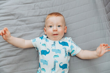 Fototapeta premium a small child is lying alone on a wide bed. the kid is looking at the camera with his legs tucked under him. top view