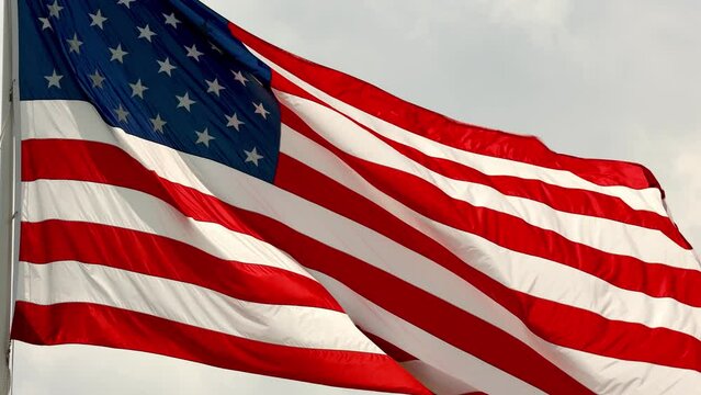 Real American flag waving in the wind, in slow motion, with vibrant red white and blue colors lit by the sun, against blue sky for copy space, 4k.