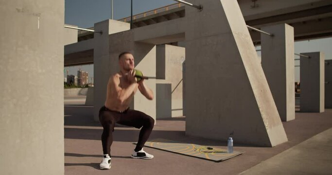 Sportsman squatting with kettlebell outdoor