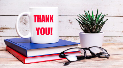 On a light table are notepads, a potted plant, black-framed glasses and a white cup with the text...
