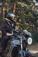 A young male biker travels on a motorcycle alone, stopped and puts on a helmet on the side of a forest road