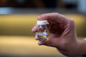 Close up of hand holding a vaccine glass bottle with isolated blur background. No label on glass bottle.
