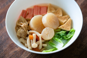 Oden (Japanese hotchpotch) in white bowl with daikon, fishcake, vegetables, cracb stick, mushroom ...