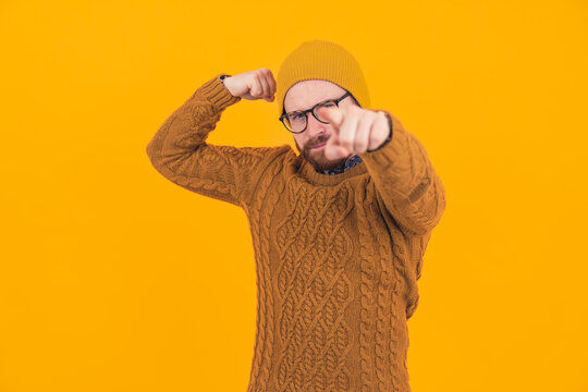Stylish hipster flexing his muscles and pointing a finger to the camera over the orange background - physical and mental strenght concept. High quality photo