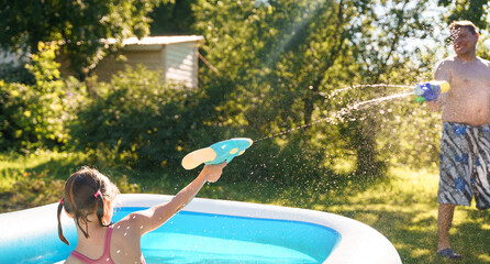 Little girl in swimwear, daughter dad, daddy, father swim, play water pistols, guns in children's...
