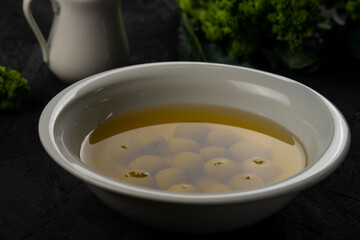 green olives in olive oil in white bowl on the black desk