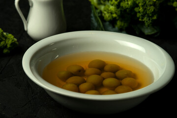 green olives in olive oil in white bowl on the black desk