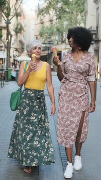 Mature female friends eating an ice cream while walking together on the street.