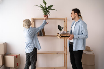 Apartment owners man and women move to a new house, unpack things put flowers on the shelf, moving and renovation