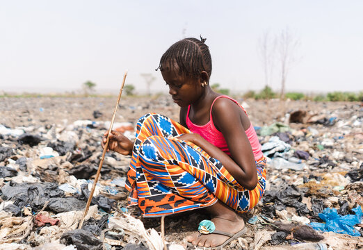 Young African girl listlessly poking through a pile of rubbish, forced to search for salable materials; concept of child labour