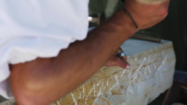 Stone carver with white shirt is hitting a stone with a hammer and a chisel at a medieval market festival called "Wallenstein" in Altdorf, Germany in slow motion