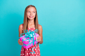Photo of thoughtful funny small girl wear pink dress holding present box looking empty space isolated turquoise color background