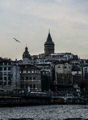 Fototapeta premium Istanbul, Turkey - April 2022: Medieval Galata Tower is famous landmark of Istanbul. Scenery of old historical place, panorama of Beyoglu district and ships on Golden Horn in the evening