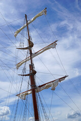 Tall ship mast with rolled sails, sky in background