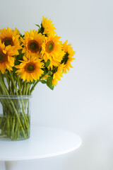 Close-up, a beautiful bouquet of traditional Ukrainian sunflower flowers in a glass vase on a white table.