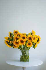 A large beautiful bouquet of traditional Ukrainian sunflower flowers in a glass vase on a white table.