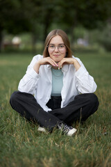 A young European girl in glasses is resting in a park on a green stave. Portrait of a girl 
