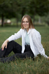 A young European girl in glasses is resting in a park on a green stave. Portrait of a girl 