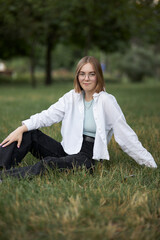 A young European girl in glasses is resting in a park on a green stave. Portrait of a girl 