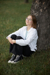 A young European girl in glasses is resting in a park on a green stave. Portrait of a girl 