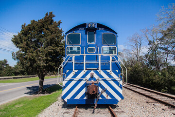 The old locomotive of the train stands on rusty rails next to the highway.