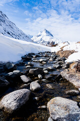 a river with stones and a lots of snow on the sides in winter, in the background a huge mountain from Galt&uuml;r