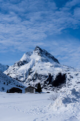 Fototapeta premium a mountain in Galtür covered in snow, in the foreground 2 huts