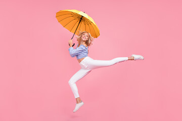 Full length photo of dreamy sweet girl dressed blue top jumping high holding umbrella isolated pink color background © deagreez