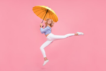 Full length photo of dreamy sweet girl dressed blue top jumping high holding umbrella isolated pink...