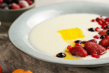 Traditional breakfast semolina porridge - creamy pudding with butter, frozen berries and fresh apricots in a grey plate