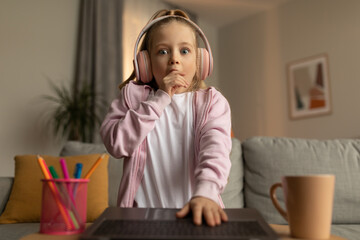 Shocked Little Girl Looking At Laptop Wearing Headphones At Home