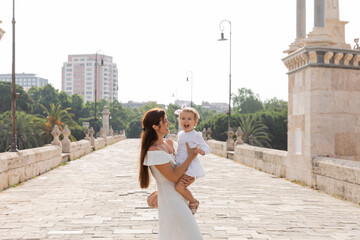 Happy mother in summer dress holding excited baby on Puente Del Mar bridge in Valencia. - Powered by Adobe