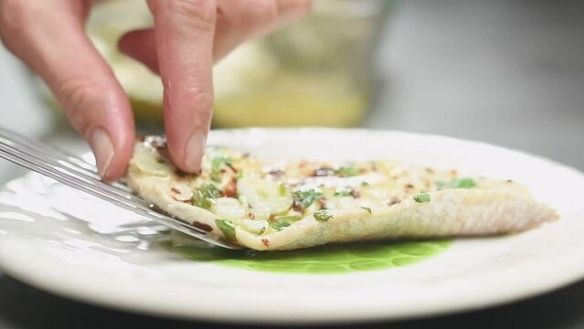 Chef serves a baked fish fillet on a plate.
