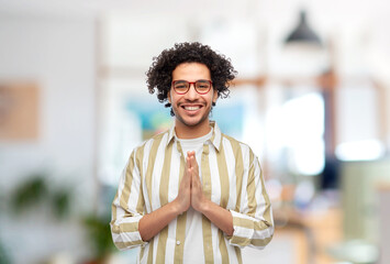 people, work and faith concept - happy smiling man in glasses making namaste gesture over office background - obrazy, fototapety, plakaty