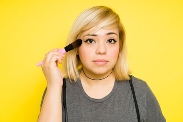 Obraz premium Closeup of a fat woman with dyed hair putting on some makeup with a brush and making eye contact