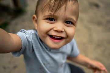 A one-year-old kid plays in a summer park on a playground, he sits in a sandbox and plays with sand - the concept of a happy carefree childhood